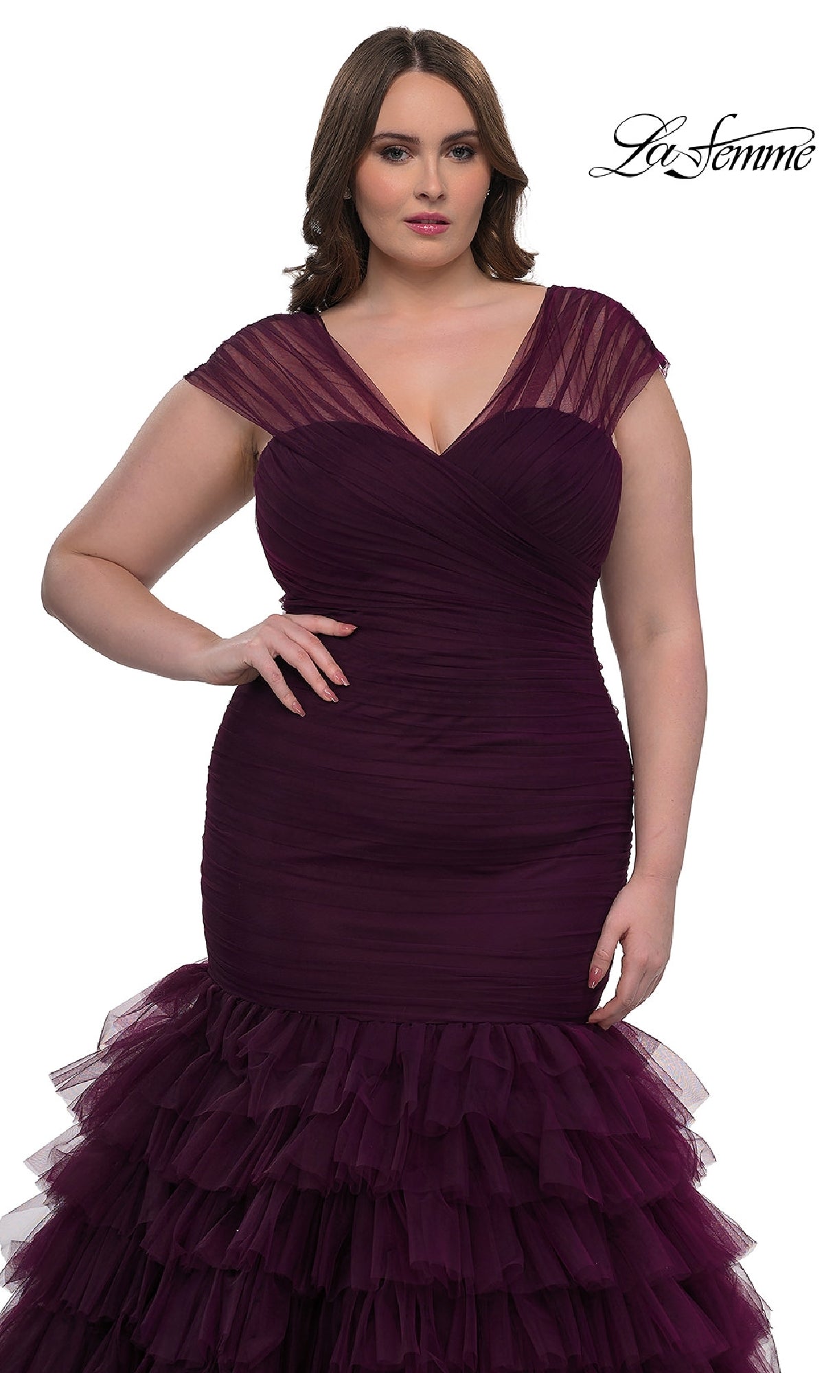 A woman wears the La Femme 32389, a plus-size long mermaid prom dress in deep purple with a ruched bodice, sheer cap sleeves, and layered ruffle skirt. The La Femme logo appears in the top right corner.
